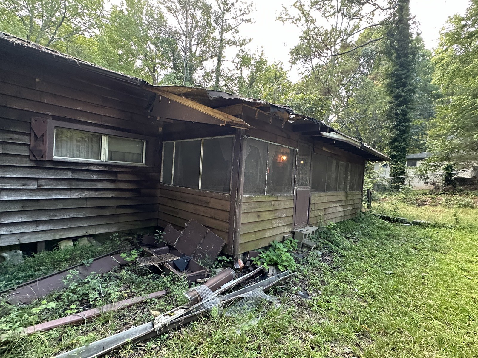 Neglected ranch exterior before renovation with weathered, rotting wood siding and debris in the yard