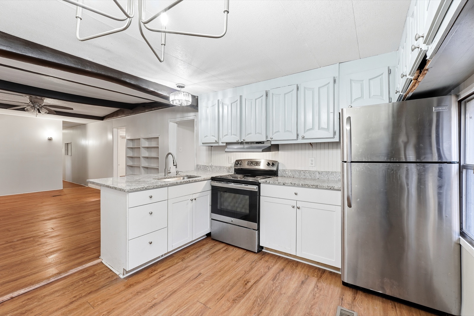 Bright renovated kitchen with white shaker cabinets, a stone-topped peninsula, and stainless appliances open to the living room