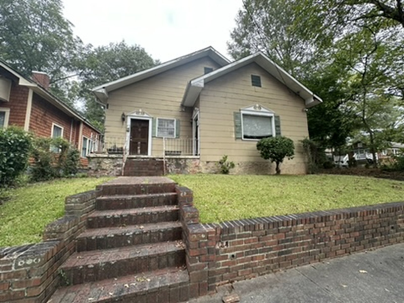 Dated home exterior before renovation with faded green siding and an overgrown yard
