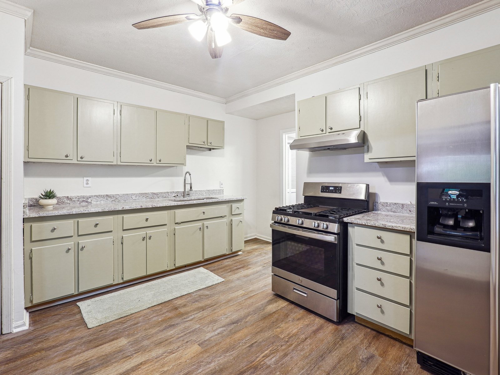 Bright renovated kitchen with white cabinets, stone countertops, stainless appliances, and new wood-look flooring
