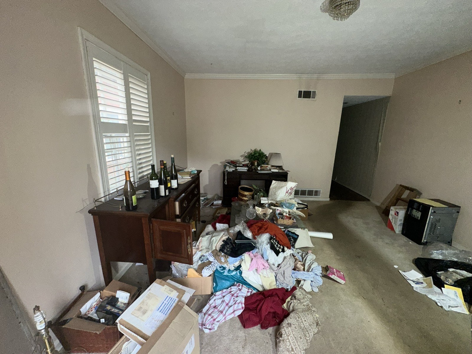 Cluttered, dated living room before renovation with worn carpet and dingy walls